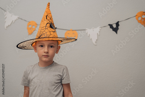 A boy in an orange Halloween hat with a spider stands on the background of Halloween decor, free space, halloween concept. High quality photo