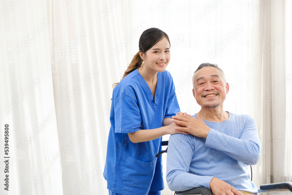 The caregiver therapist stands with an Asian senior sitting in a wheelchair and touches their hands on senior shoulder together. The nursing home facilitates a support group. Image with copy space The caregiver therapist stands with an Asian senior sitting in a wheelchair and touches their hands on senior shoulder together. The nursing home facilitates a support group. Image with copy space