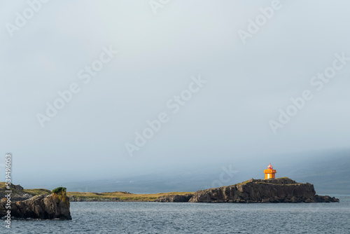 The bright-orange Aeoarstein Lighthouse in Djupivogur, east Iceland, sits atop harsh volcanic rock photo