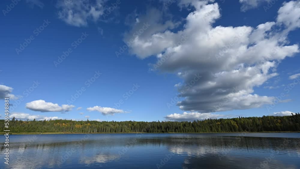 Time lapse of white clouds in a blue sky moving above a large lake with a forest along the shore
Time lapse of white clouds in a blue sky moving above a large lake with a forest along the shore