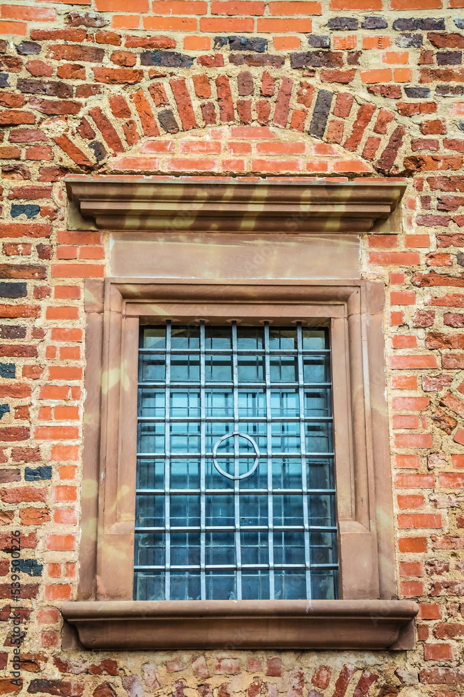 Brick wall of an old building with a window with a lattice