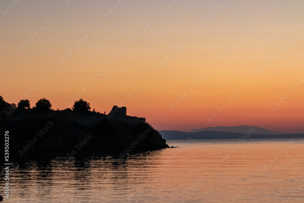 Silhouette of ruin with panoramic view of sunset over Aegean Mediterranean Sea seen from Karydi beach, peninsula Sithonia, Chalkidiki (Halkidiki), Greece, Europe. Romantic atmosphere, water reflection