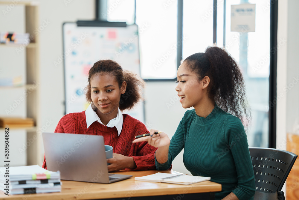 Focused young african american businesswoman or student looking at laptop holding book learning, serious black woman working or studying with computer doing research or preparing for exam online Focused young african american businesswoman or student looking at laptop holding book learning, serious black woman working or studying with computer doing research or preparing for exam online