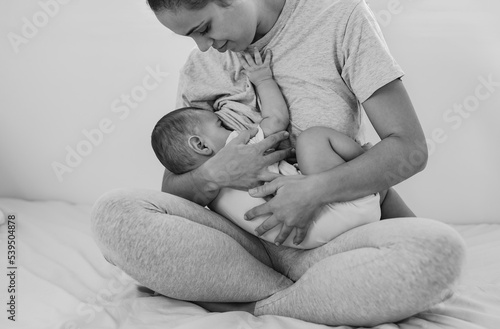 Young loving mother breastfeeding her baby at home wile sitting on bed
