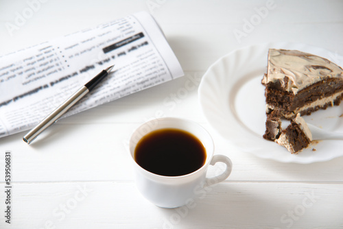 businessman breakfast. on the table a cup of coffee  a piece of cake  a newspaper and a pen.