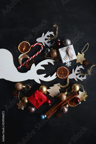 Small presents, various Christmas ornaments and deer figurine on dark background. Top view.