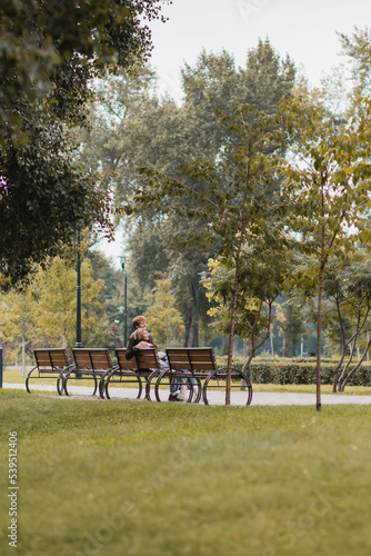 happy young man and woman hugging and sitting on wooden bench in green park.