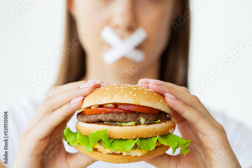 Portrait of a woman who wants to eat a burger, but her mouth is taped
