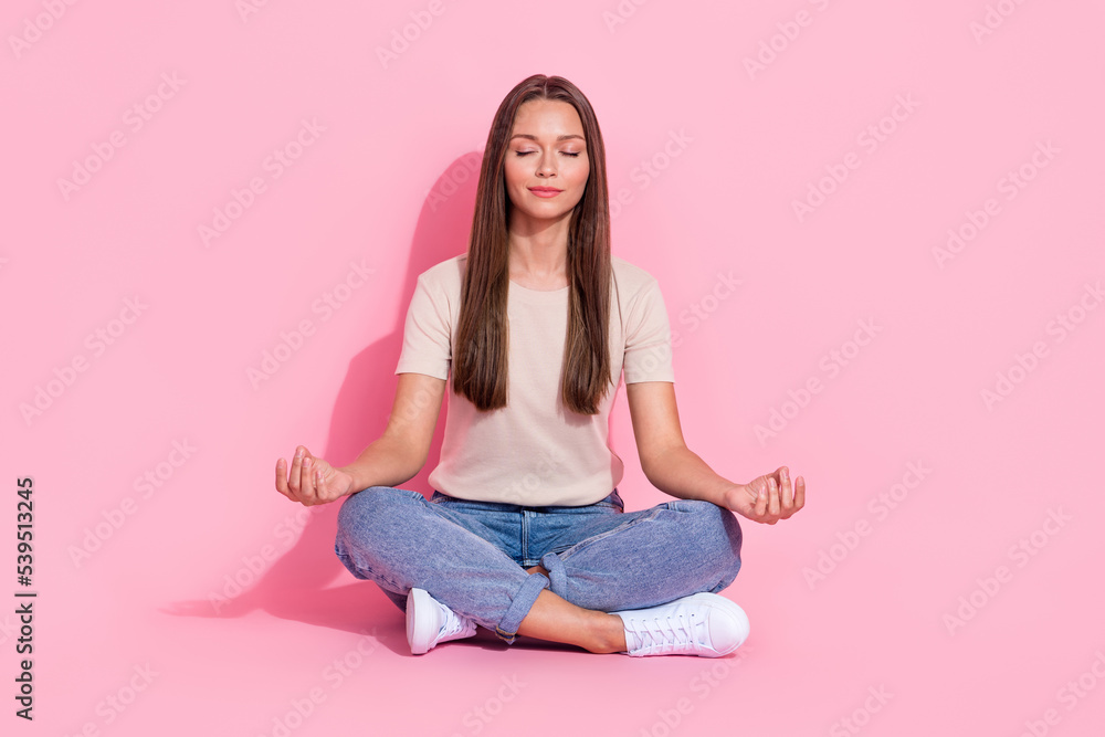 Full length photo of funny dreamy lady wear beige t-shirt sitting legs crossed practicing yoga isolated pink color background Full length photo of funny dreamy lady wear beige t-shirt sitting legs crossed practicing yoga isolated pink color background