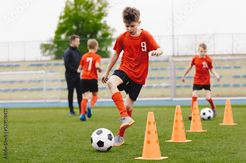 Training football session for children on soccer camp. Boy in children s soccer team on training. Kids practicing outdoor with a soccer balls. Young boy improving dribbling skills. Training with cones
