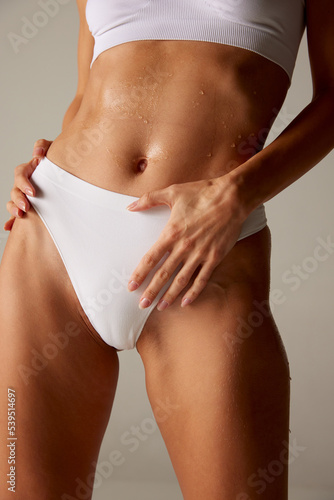 Cropped image of tanned female body, belly in white underwear with water drops isolated over grey background photo