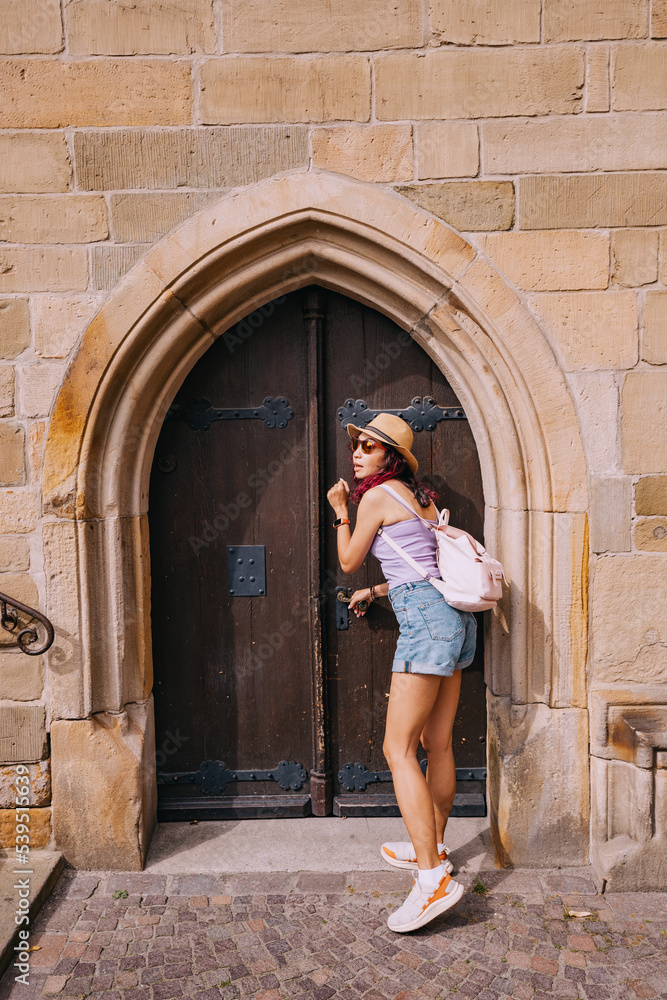 tourist girl enters the arch door portal of a small chapel or church in the old town square