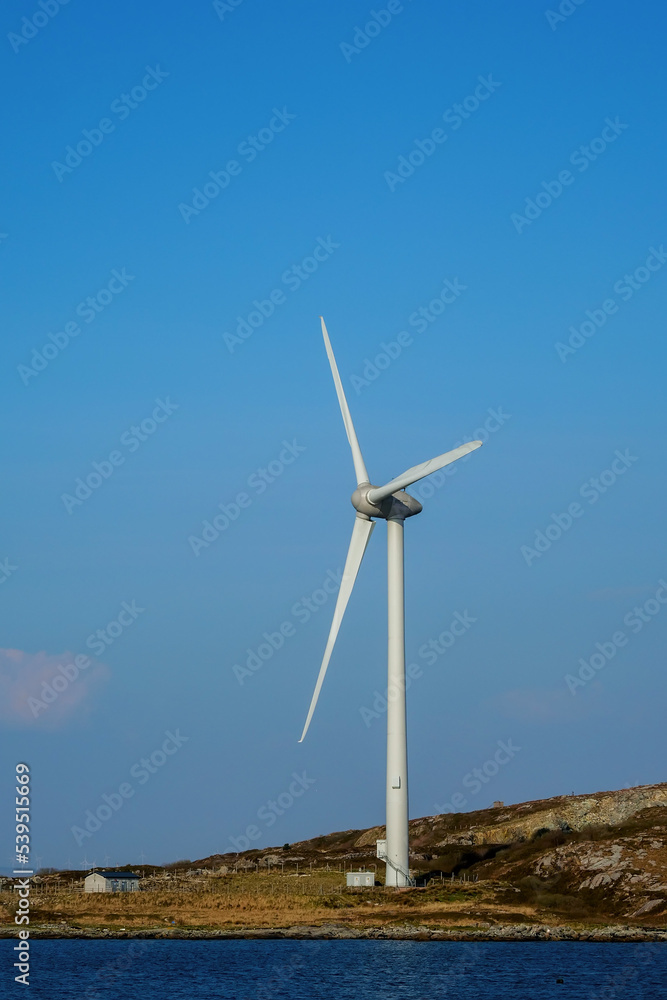 One wind turbine installed by the ocean. Clean blue sky and water surface. Alternative energy source in time of fuel and gas crisis. Production of green clean power. One wind turbine installed by the ocean. Clean blue sky and water surface. Alternative energy source in time of fuel and gas crisis. Production of green clean power.