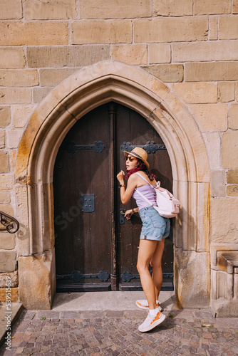 tourist girl enters the arch door portal of a small chapel or church in the old town square © EdNurg