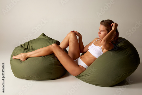 Portrait of beautiful woman lying on big pillows in white underwear isolated over grey background. Sportive body