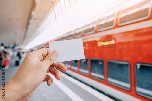 Credit or prepaid transport card in the passenger's hand against the background of a modern double-decker high-speed train on the platform of the railway station photo