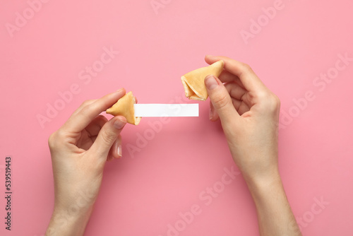 Woman holding tasty fortune cookie and paper with prediction on pink background, top view. Space for text