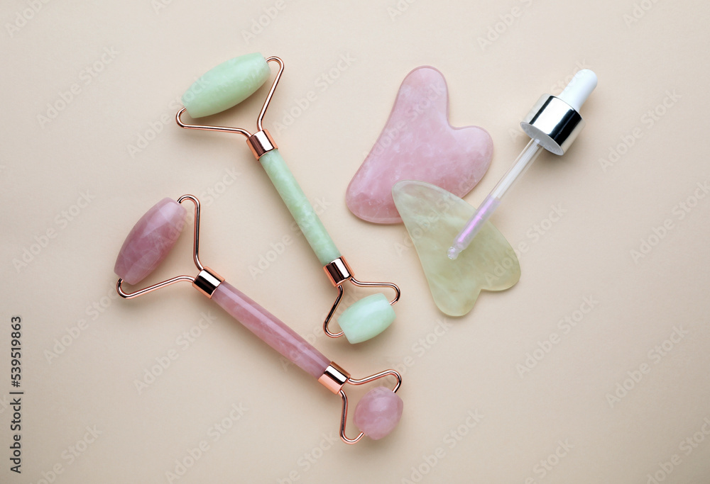 Gua sha tools, facial rollers and dropper on beige background, flat lay Gua sha tools, facial rollers and dropper on beige background, flat lay