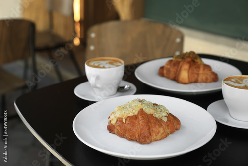 Tasty croissants and cups of aromatic coffee on black table in cafeteria