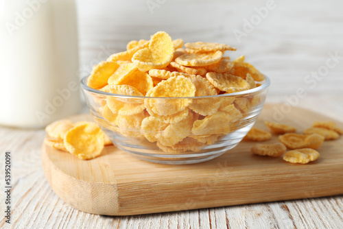 Glass bowl of tasty crispy corn flakes on white wooden table