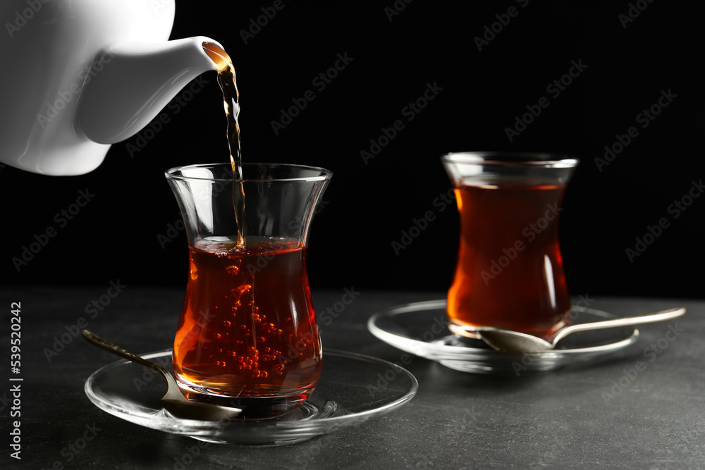 Pouring traditional Turkish tea from pot into glass on black table, closeup Pouring traditional Turkish tea from pot into glass on black table, closeup