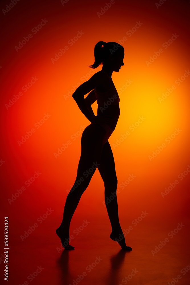 Silhouette of female full-length body isolated over orange background. Side view.