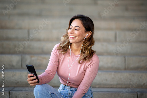young woman sitting on stairs with mobile phone listening to music
