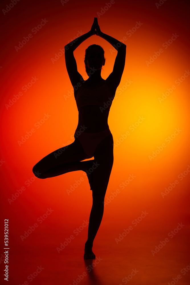Silhouette of female full-length body isolated over orange background. Standing on yoga pose