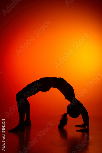 Silhouette of female full-length body isolated over orange background. Standing on bridge yoga pose