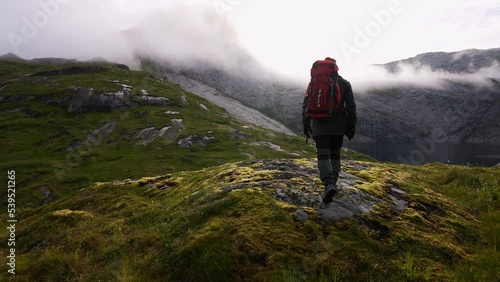 Young man standing at famous cliff edge and enjoying a scenic view over a valley, lake and the mountains in Lofoten Islands, Norway near Munken and Munkebu. photo