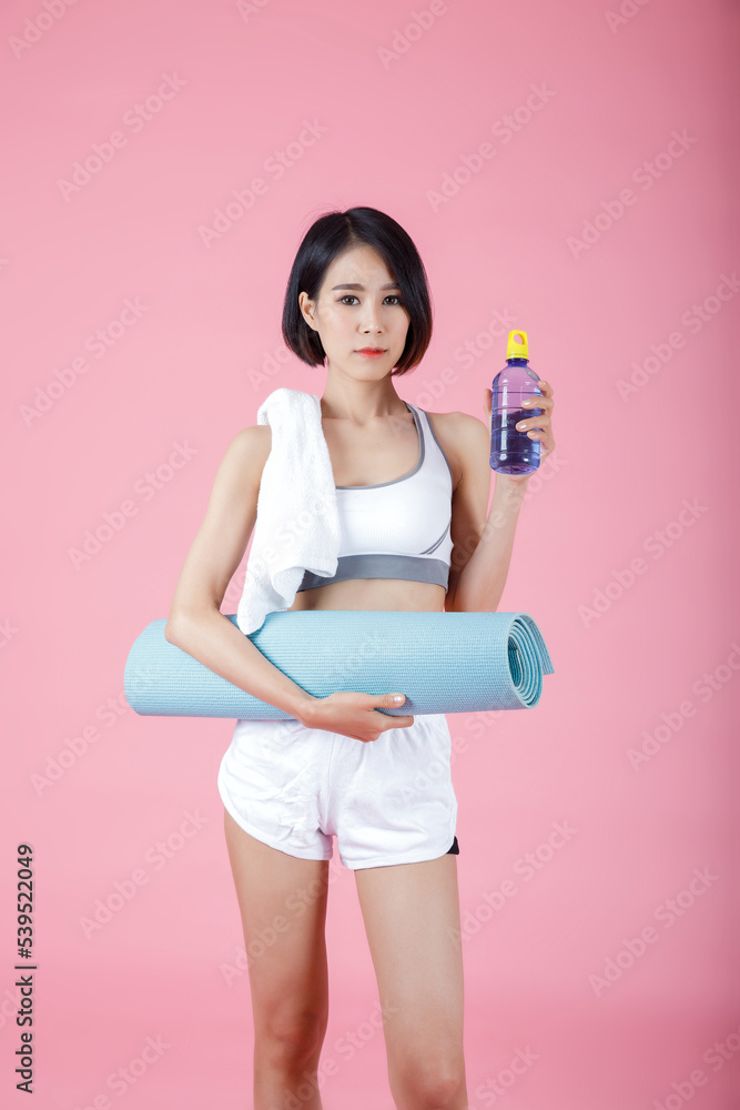 Portrait of woman holding exercise mat roll and drinking water bottle, holding yoga mat roll on pastel pink background. Portrait of woman holding exercise mat roll and drinking water bottle, holding yoga mat roll on pastel pink background.