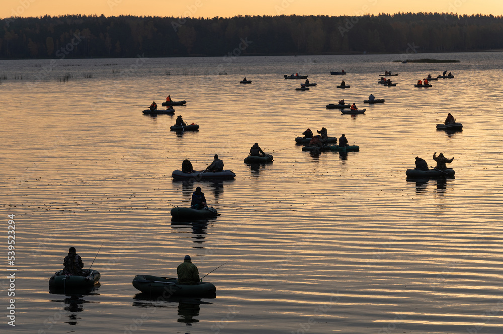 Two or three dozen fishermen, at the same time, on inflatable rubber boats, gathered in one place for fishing. River, lake, reservoir. Sunrise.At anchor. Two or three dozen fishermen, at the same time, on inflatable rubber boats, gathered in one place for fishing. River, lake, reservoir. Sunrise.At anchor.