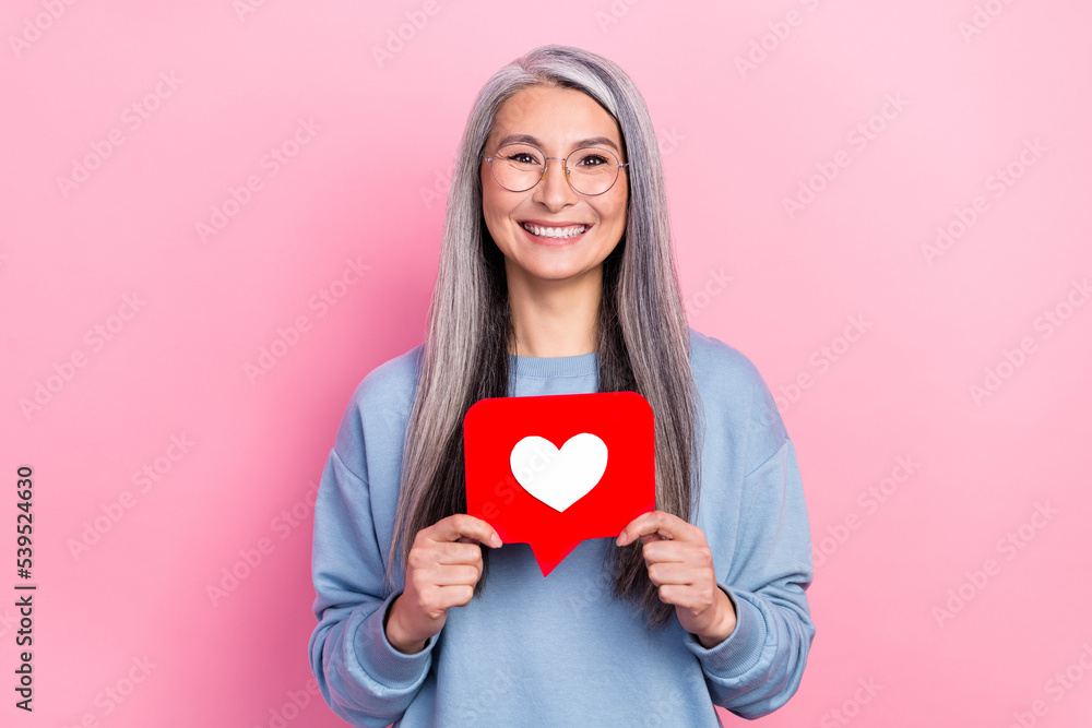 Portrait of attractive cheerful grey-haired woman granny holding like card isolated over pink pastel color background Portrait of attractive cheerful grey-haired woman granny holding like card isolated over pink pastel color background