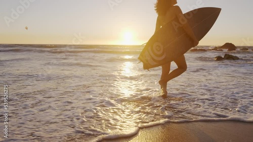 The young female surfer walks on the beach with a surfboard in her hand. Sunset at the ocean. Healthy sport.