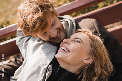 cheerful and redhead man looking at happy blonde woman smiling in park.
