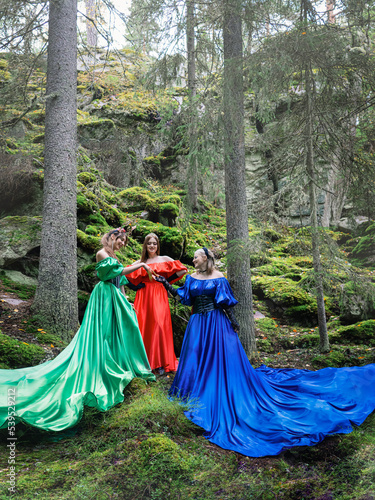 Three beautiful girls in long dresses on the background of the forest. Forest nymphs.