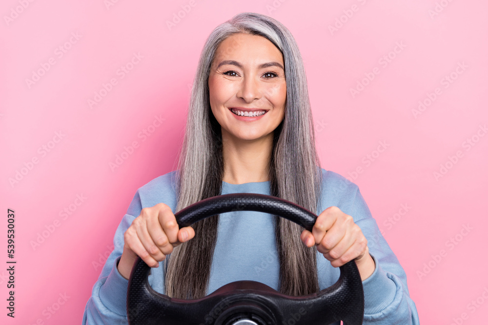 Photo of cheerful positive retired woman blue sweater riding vehicle holding steering wheel isolated pink color background Photo of cheerful positive retired woman blue sweater riding vehicle holding steering wheel isolated pink color background