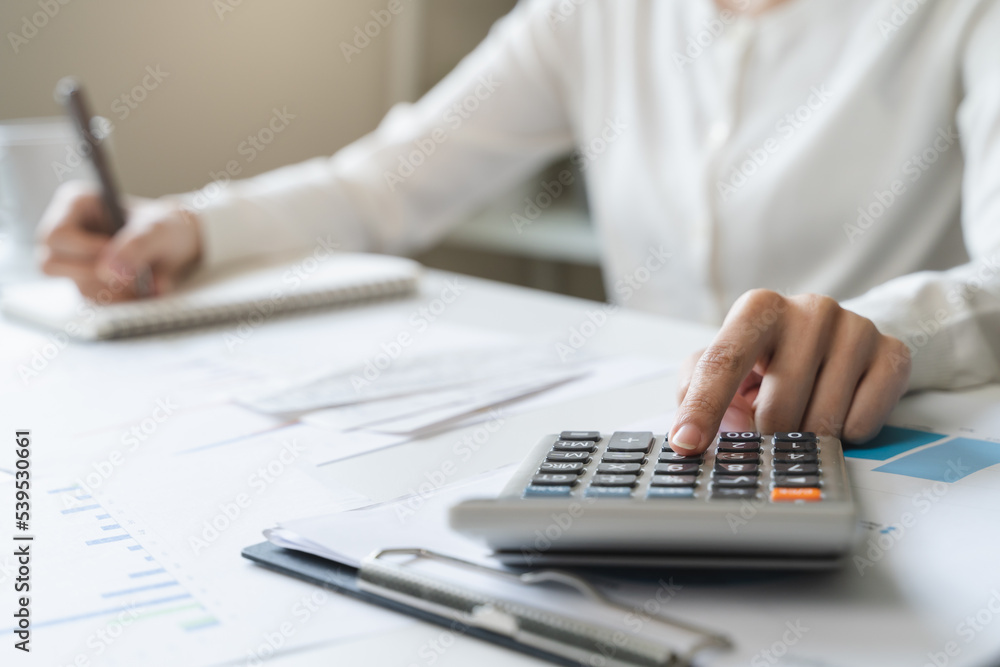 Women business people use calculators to calculate the company budget and income reports on the desk in the office. Women business people use calculators to calculate the company budget and income reports on the desk in the office.