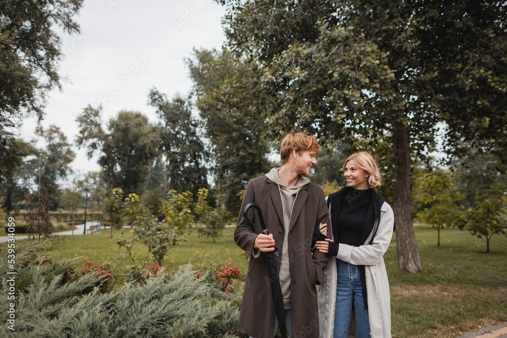happy blonde woman hugging cheerful redhead boyfriend with umbrella in park. happy blonde woman hugging cheerful redhead boyfriend with umbrella in park.