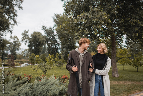 happy blonde woman hugging cheerful redhead boyfriend with umbrella in park. © LIGHTFIELD STUDIOS