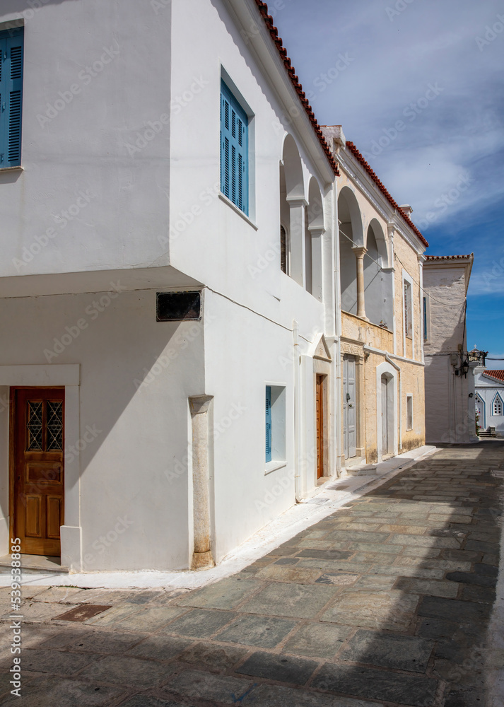 Greece. Andros island Chora town Cyclades. Cobblestone alley old houses sun blue sky. Vertical