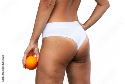 Young woman in white uderwear with cellulite and white stretch marks from a weight loss or weight gain on thighs holding orange in her hand isolated on a white background. Excess weight, overweight