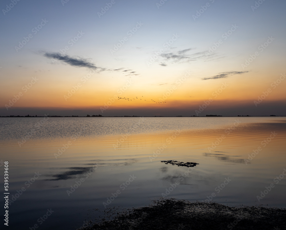 Serene landscape in a lagoon during the arrival of twilight. Golden colors in the sky reflected in the water.