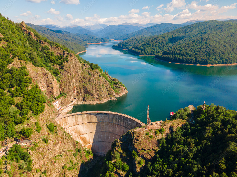 Aerial photography of Vidraru dam, in Romania. Photography was shot from a drone from above canyon at Vidraru lake with the dam and the lake in the view and mountains in the background.
