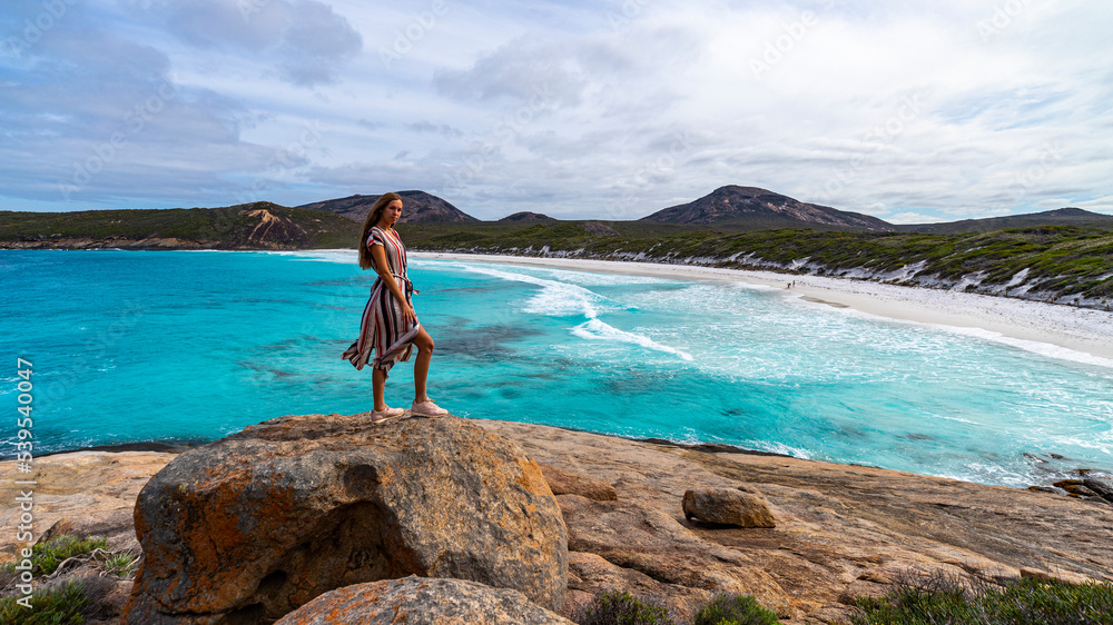 girl in long dress stands on rocks admiring the power of the ocean; amazing beach with turquoise water, hellfire bay near esperance in western australia