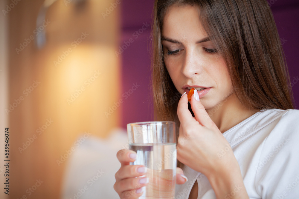 Happy woman taking vitamin pills in the morning on a bed at home Happy woman taking vitamin pills in the morning on a bed at home