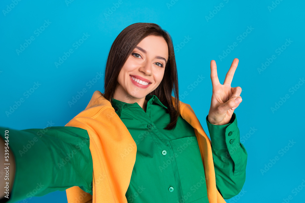 Photo of pretty positive person make selfie demonstrate v-sign isolated on blue color background Photo of pretty positive person make selfie demonstrate v-sign isolated on blue color background