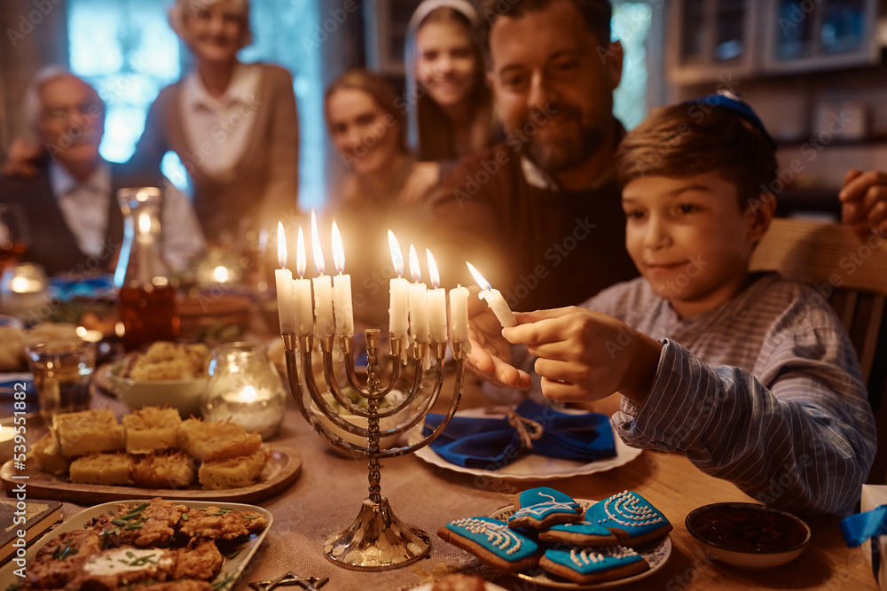 Jewish son and father lighting menorah during family meal on Hanukkah.