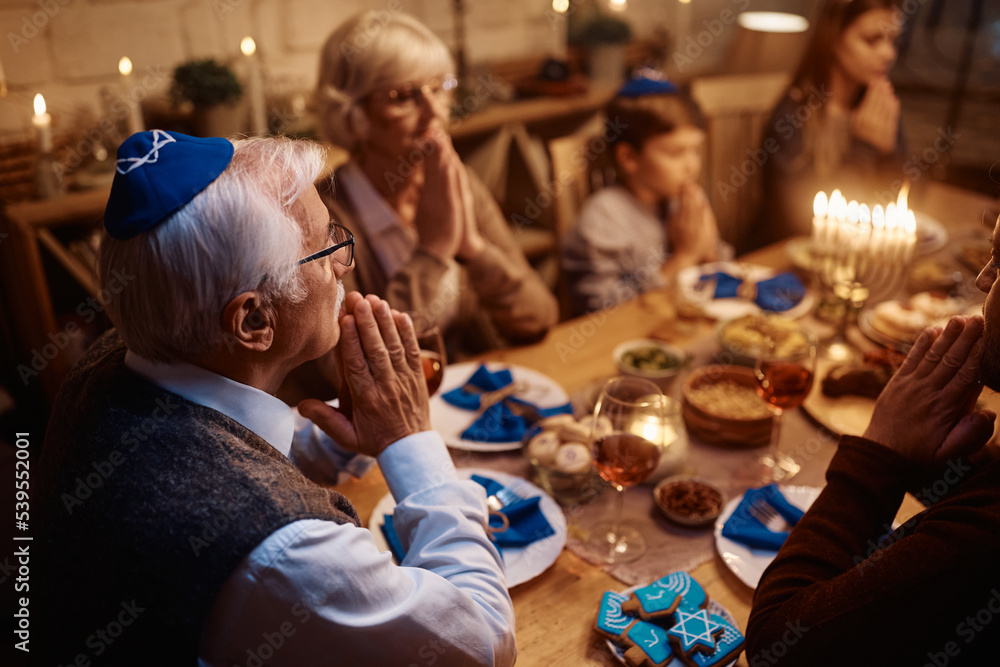 Multigeneration Jewish family praying during meal at dining table on Hanukkah.