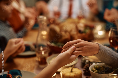 Close up of mother and daughter holding hands during family prayer on Thanksgiving at dining table.